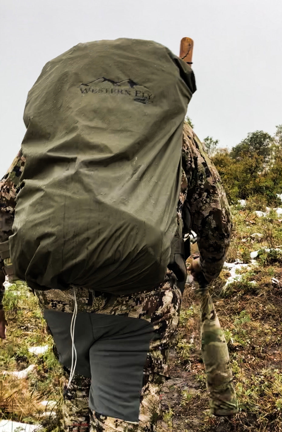 Person wearing an olive green Western Fly pack fly over camouflage clothing in an outdoor setting