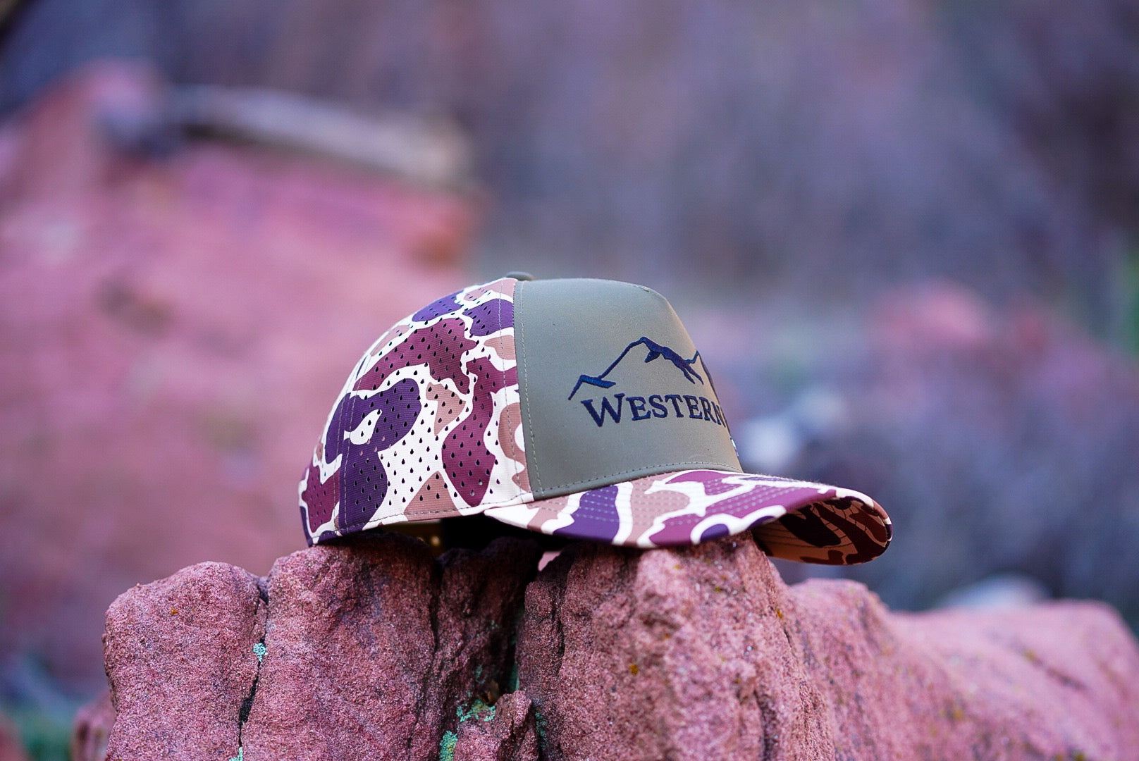 Camouflage-patterned hat with 'Western' logo on a rock against a blurred natural background