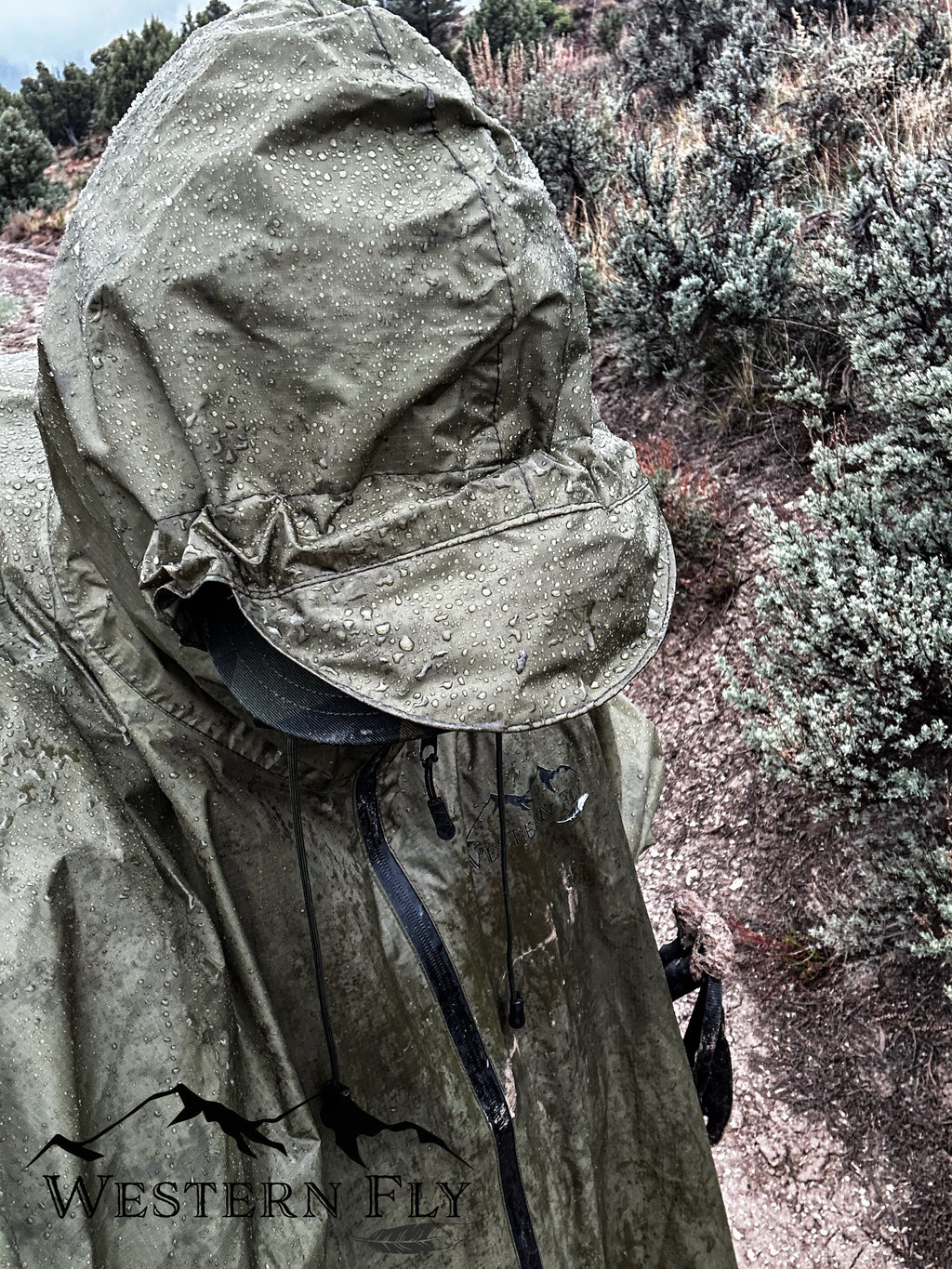 Person wearing a green Western Fly poncho with a hood in a natural setting