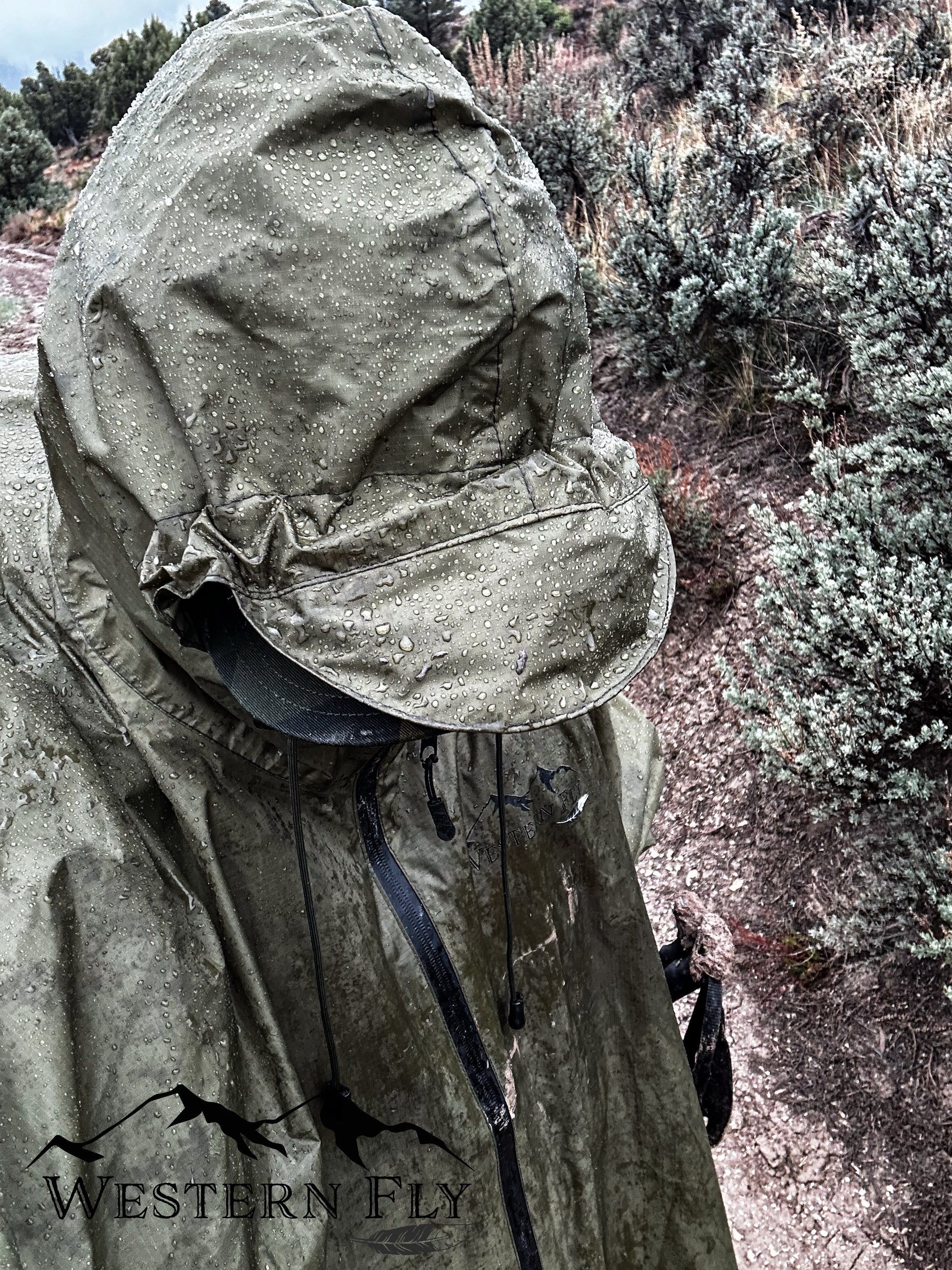 Person wearing a green Western Fly poncho with a hood in a natural setting