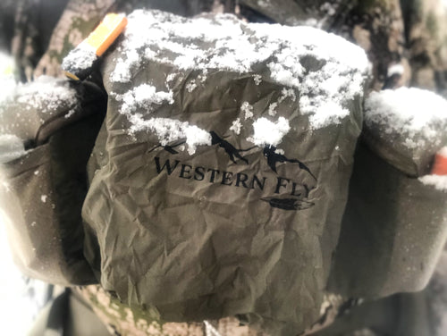 Snow-covered olive drab bino fly with 'Western Fly' logo on a blurred natural background